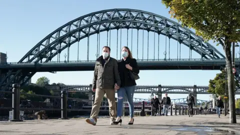 PA Media Couple wearing masks walking along Newcastle Quayside with Tyne Bridge in the background