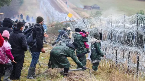 Getty Images Migrants stand near a barbed-wire fence