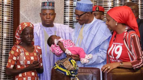 AFP Nigerian President Mohammadu Buhari (C) flanked by Borno state governor Kashim Shettima (L) and Chief of Staff for the Kaduna State Governor Hadiza Bala Usman (R) carries Amina Ali's four-month-old baby on her arrival at the presidency in Abuja, on May 19, 2016