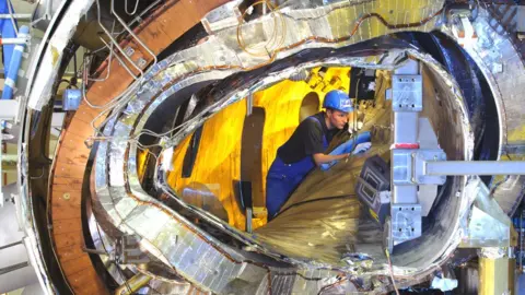 MPI View inside one of the W7X modules. Visible are the plasma vessel, a magnet coil, the outer casing, and numerous ducts for coolant and leads for power