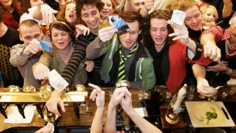 Getty Images Drinkers in a busy pub try and get bartender's attention