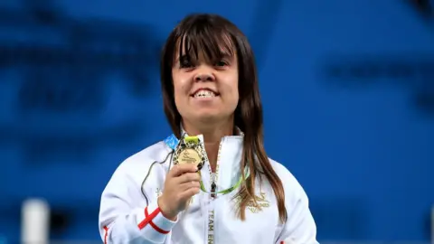 PA Media Zoe Newson in an white England branded zip up top. Ms Newson is holding a Gold commonwealth medal and smiling.