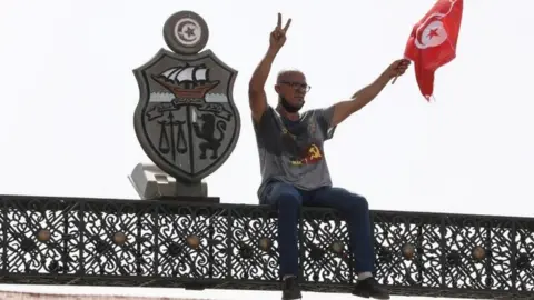 A protester sits on top of a gate outside the parliament building in Tunis, Tunisia. Photo: 26 July 2021