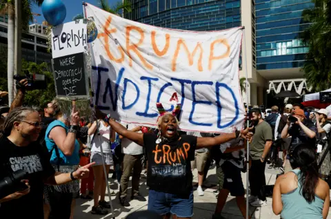 Reuters A person holds a banner near The Wilkie D. Ferguson Jr. United States Courthouse, on the morning former U.S. President Trump is to appear there on classified document charges, in Miami, Florida, U.S., June 13, 2023