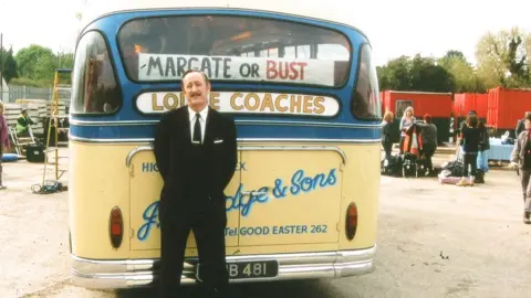 Lodge Coaches Nicholas Lyndhurst on the set of Rock and Chips standing in front of a bus