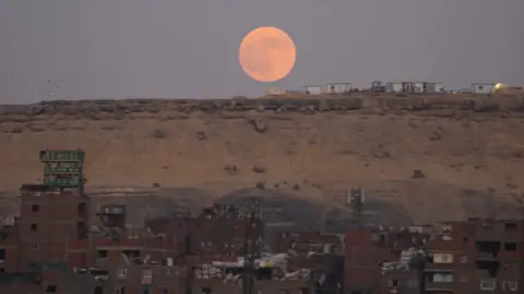 Emad Karim A picture sent by Emad Karim in Cairo, Egypt shows a glowing orange moon above reddish Egyptian sands