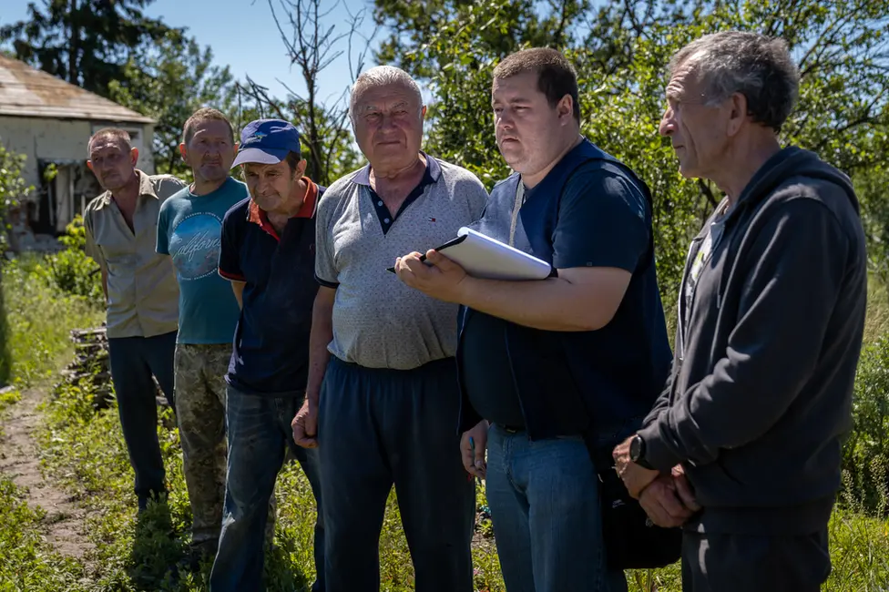 BBC Vadym Bobaryntsev, right, watches on with other villagers as a member of the prosecutor's team takes notes in Mala Rohan.