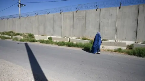 AFP via Getty Images An Afghan clad-burqa woman walks along a road outside a US military base in Bagram on July 1, 2021