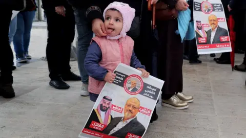 EPA A child holds photos of slain Saudi journalist Jamal Khashoggi as people gather to perform an absentee funeral prayer at Fatih Mosque in Istanbul, Turkey, 16 November 2018