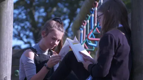 Two girls reading a book in the park