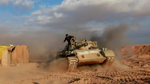 Reuters Iran-backed Popular Mobilisation paramilitary fighters ride in a tank near the Iraq-Syria border (26 November 2018)