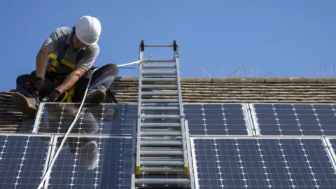 Getty Images Man installing a solar panel on a roof