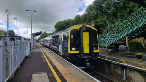 BBC a black, navy and yellow South Western Railway train at the platform at Templecombe Station