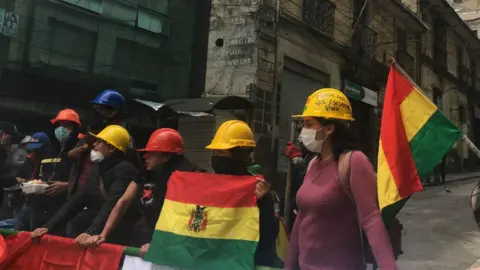 BBC A group of protesters wearing hard hats man a barricade near Mr Morales' home and office