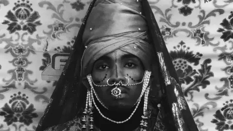 Africa Fashion at the V&A Self portrait of a man wearing traditional Ethiopian attire. He has on face jewellery and a head dress.