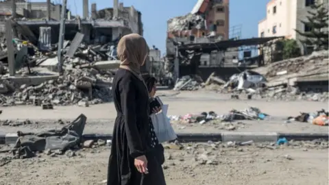 EPA A woman and girl walk past destroyed residential buildings in Al Nuseirat refugee camp