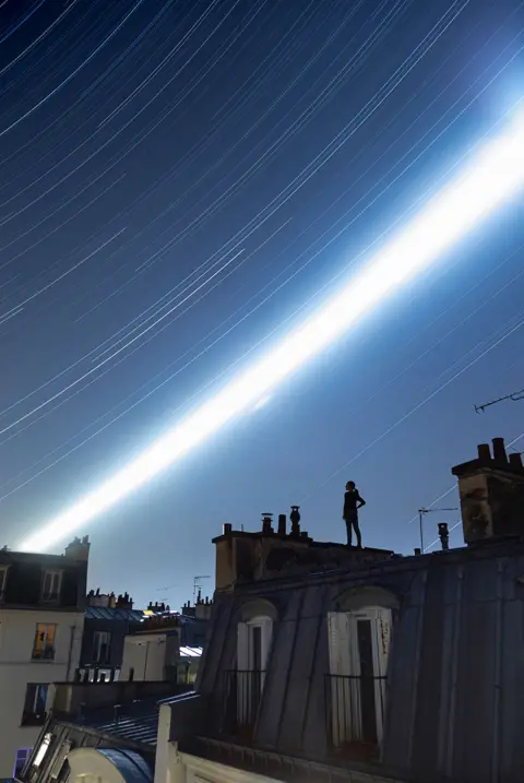 Remi Leblanc-Messager An image showing a woman standing on a Parisian rooftop with a long exposure view of the night sky