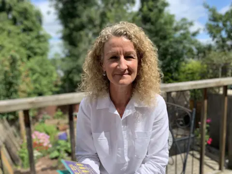 Lady in a white shirt and with curly blonde hair sat in her garden