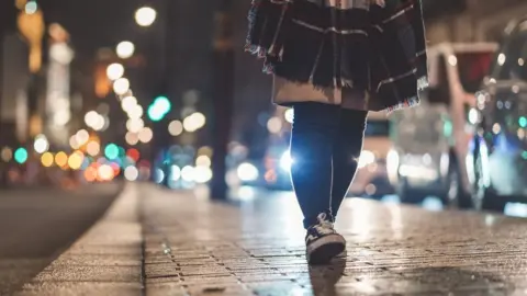 Getty Images A woman walking at night along a street lit by street lamps