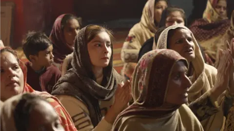 Kamil Khan Women and children sit on the floor clapping hands at Christmas carol concert