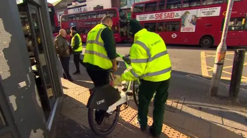 BBC Wandsworth council staff seize a lime bike and move it towards a van to be taken away.