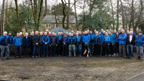 Cockermouth MRT A large group of people in blue coats pose for a picture