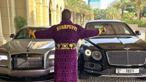 hushpuppi Hushpuppi in a monogrammed dressing gown by some luxurious cars