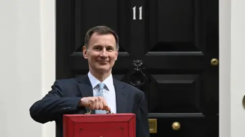 BBC Chancellor Jeremy Hunt holds up his budget red box in front of the door of Number 11