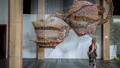 Annika Hammerschlag A viewer looking at the artwork of Ngozi Ezema, which looks like a teapot suspended in mid-air.