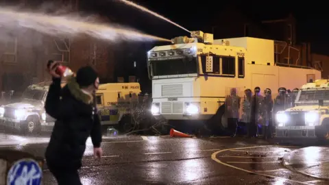 PA Media Objects are thrown towards PSNI officers and the water canon on Springfield Road in Belfast during further unrest