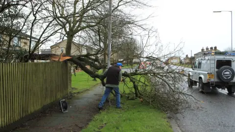 PA Media A man works to remove a tree blown over by Storm Dennis in Birkenshaw on the outskirts of Bradford