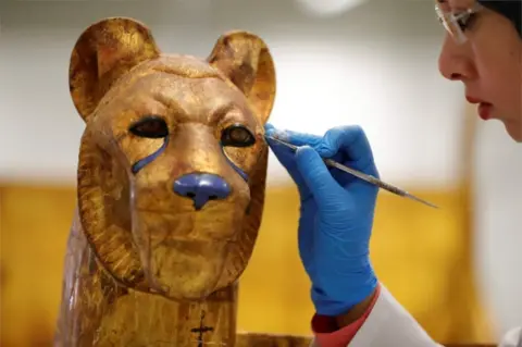 AFP A gloved specialist uses an implement to restore the surface of a golden cat-like figure.
