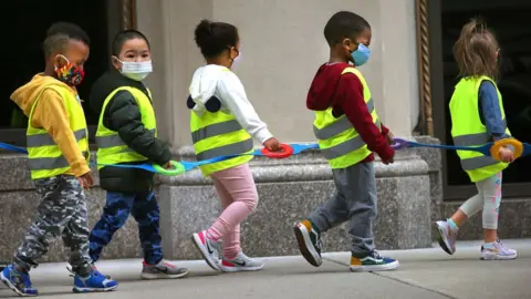 The Boston Globe via Getty Images Youngsters in a preschool class wear vests and masks and hold on to a strap as they take a walk outdoors in Boston