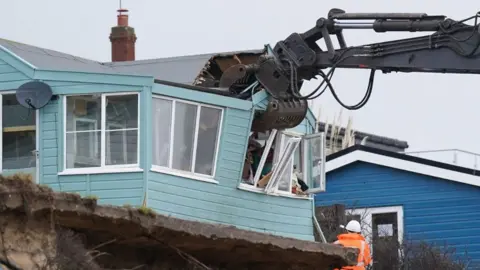 Joe Giddens/PA High-reach grab demolishing a wooden bungalow in Hemsby