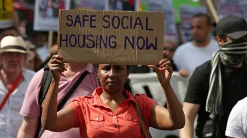 Getty Images woman holds placard reading 'safe social housing now'