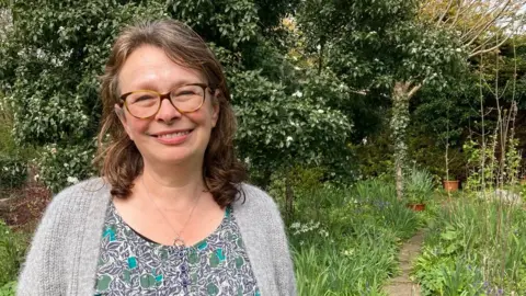 Bespectacled Andrea Skevington smiling in her garden.