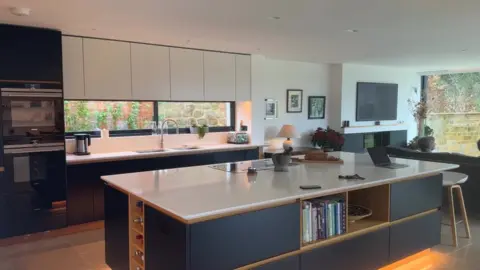 Luis Timms/BBC Modern kitchen area with modern units, central bar area and long window