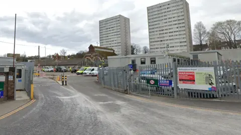 Google Waste depot in Hollingdean - a gate with signs and two tower blocks in the background