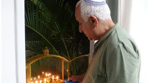 Shai's father Dror looking pensive as he lights candels