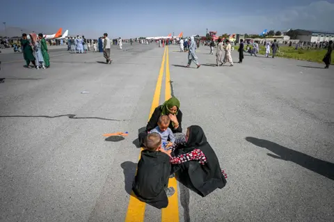 AFP Afghan people sit on the tarmac as they wait to leave the Kabul airport in Kabul on 16 August 2021