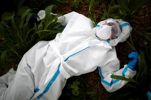 ADNAN ABIDI/Reuters A health worker wearing protective clothing rests on the ground in India