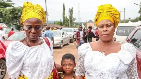 BBC Two women in headwraps with a little boy in a street of Arondizuogu during the Ikeji Festival in Nigeria