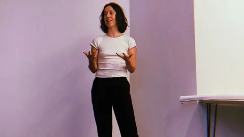 SLEEC Meggan Baker talking in a white top and dark trousers