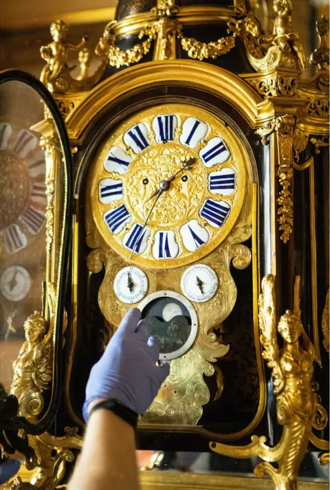 Antonio Olmos A close-up of Fjodor changing the time on a gold-decorated clock with a dial for moon changes