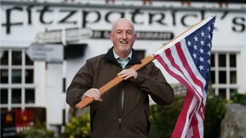 PA Media John Owen Finegan waves a US flag outside a bar in County Louth