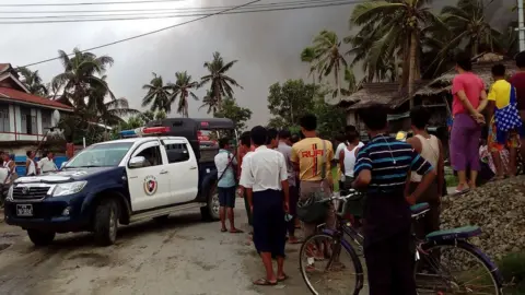 AFP This picture taken on 27 August 2017 shows a police vehicle and people next to houses burnt in Maungdaw township in Rakhine State in Myanmar