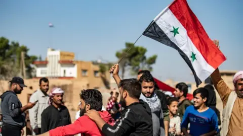 AFP Locals welcome Syrian regime forces as they arrive at the western entrance of the town of Tal Tamer