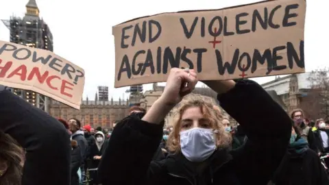 Getty Images A woman holds a placard saying end violence against women