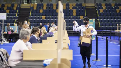 PA Media Bottles of hand sanitiser are handed out as counters sit apart, with screens separating them