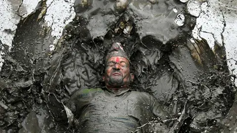A mud-covered farmer plays in a rice paddy field during National Paddy Day, which marks the start of the annual rice planting season, in Tokha village on the outskirts of Kathmandu, Nepal, on 19 June 2022